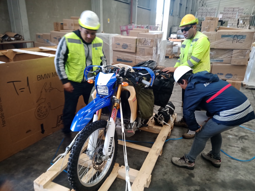 A motorcycle tied to a crate is  inspected by a customs agent